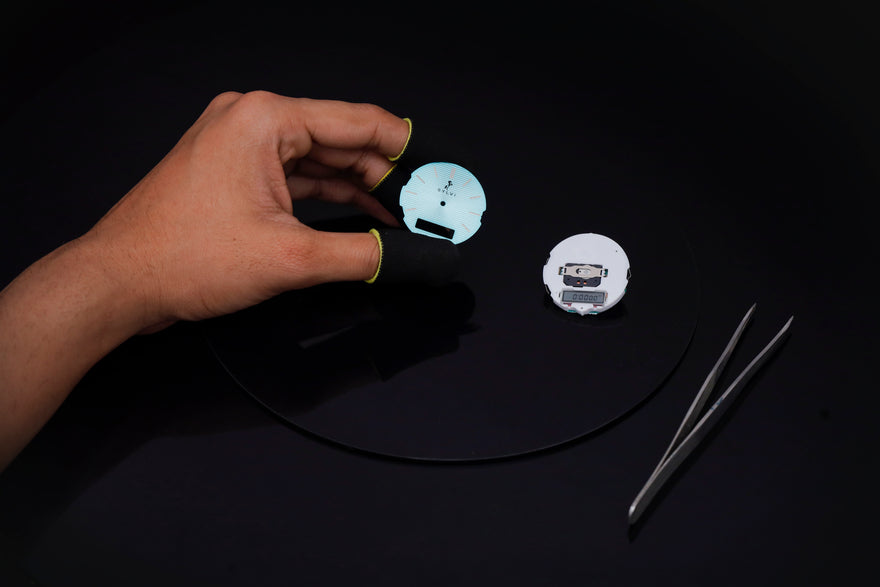 Hand holding a small round object with a design on a dark surface, with tweezers nearby.