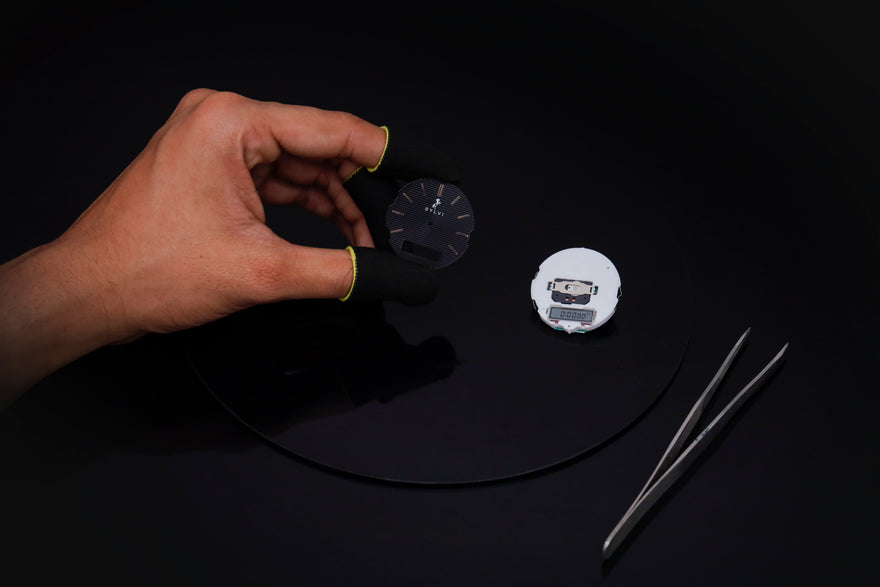 Hand holding a black circular object with two other objects on a black background
