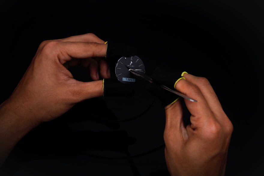 Person holding a small metallic object with tweezers against a dark background