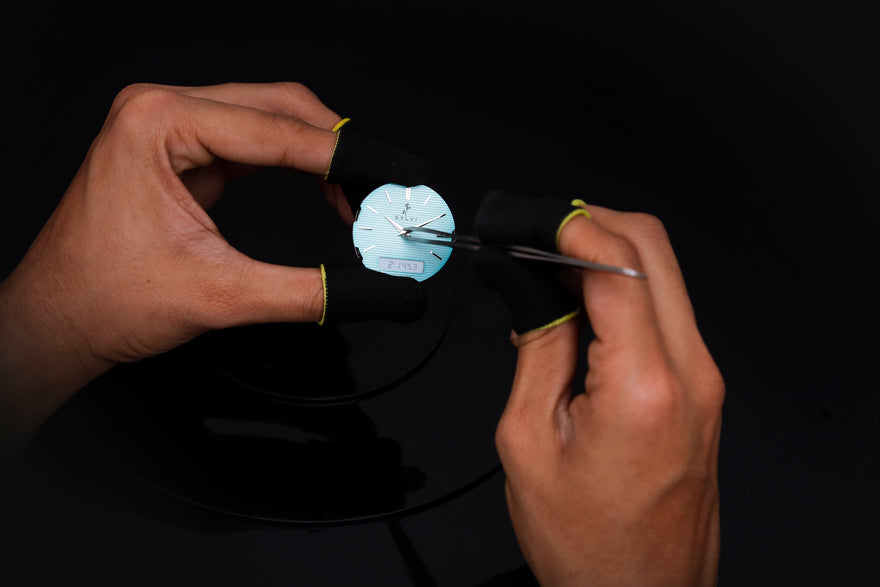 Person using tweezers to handle a small white object on a black surface