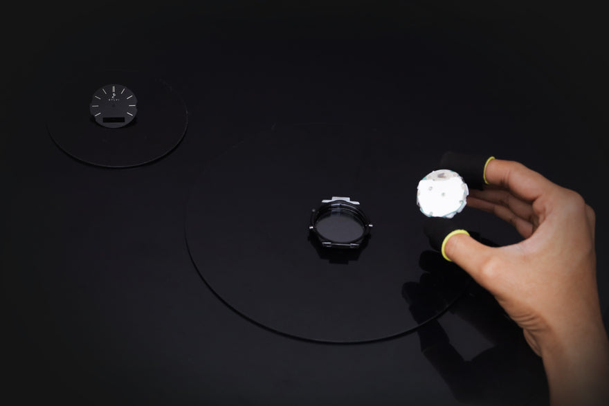 Hand holding a flashlight on a black surface with circular objects.