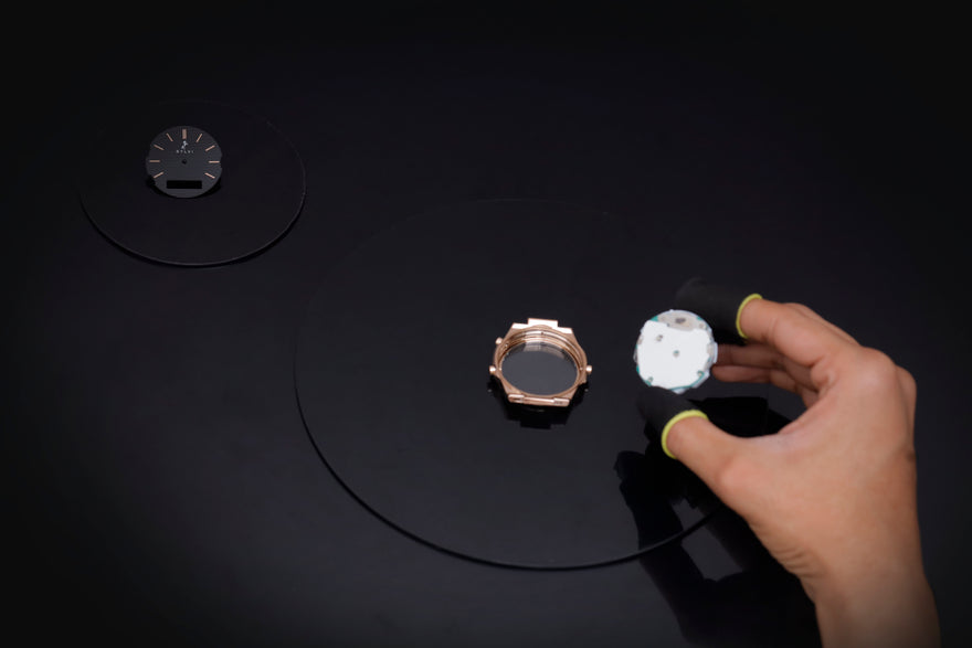 Hand holding a white object on a black surface with other objects.
