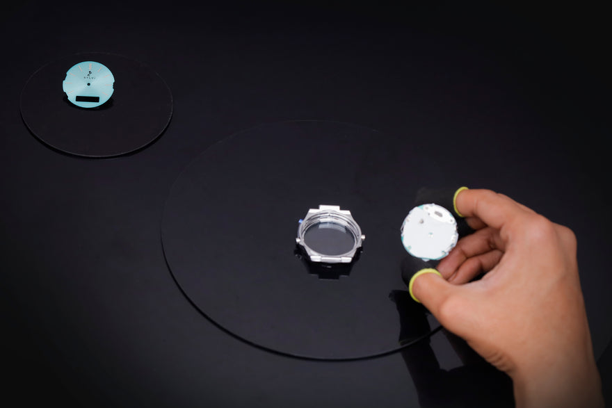 Hand holding a small white object on a dark surface with other objects.