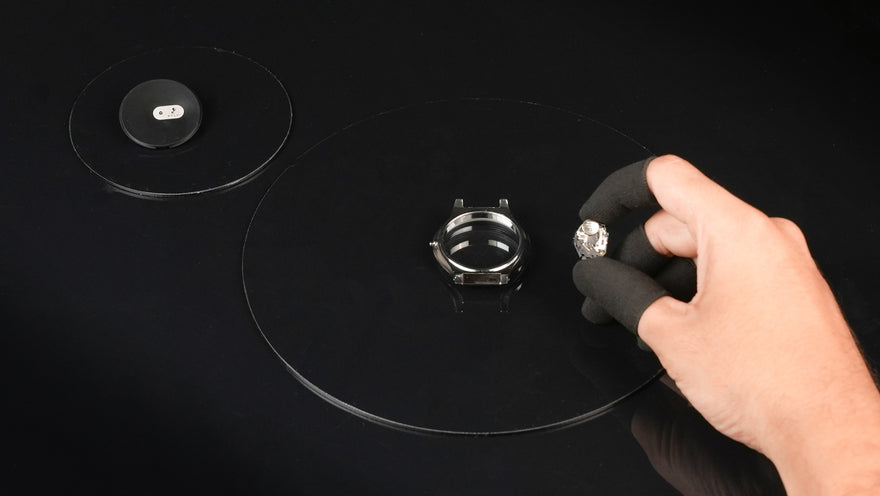 Hand holding a small metal object on a black surface with another similar object nearby.