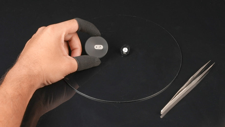 Hand holding a turntable needle over a record with tweezers on a dark background