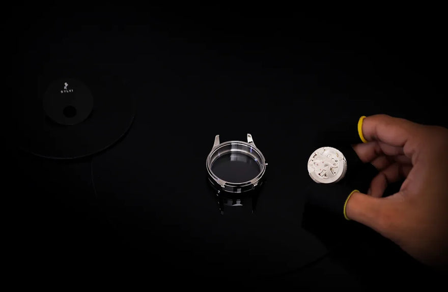 Hand holding a small white object next to a metallic ring on a black background