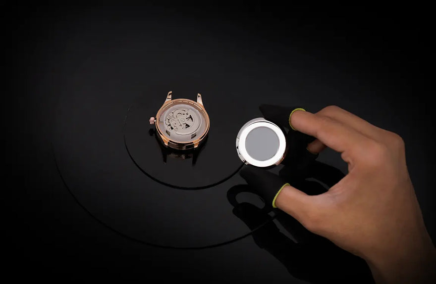 Hand using a magnifying glass to inspect a mechanical watch on a dark surface