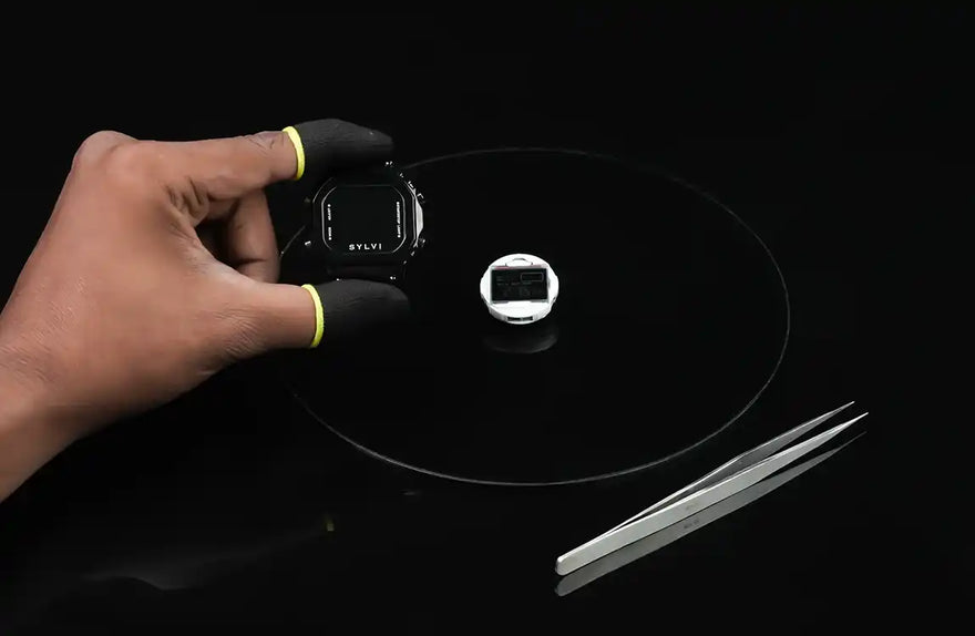 Hand holding a small electronic device on a dark surface with tweezers nearby